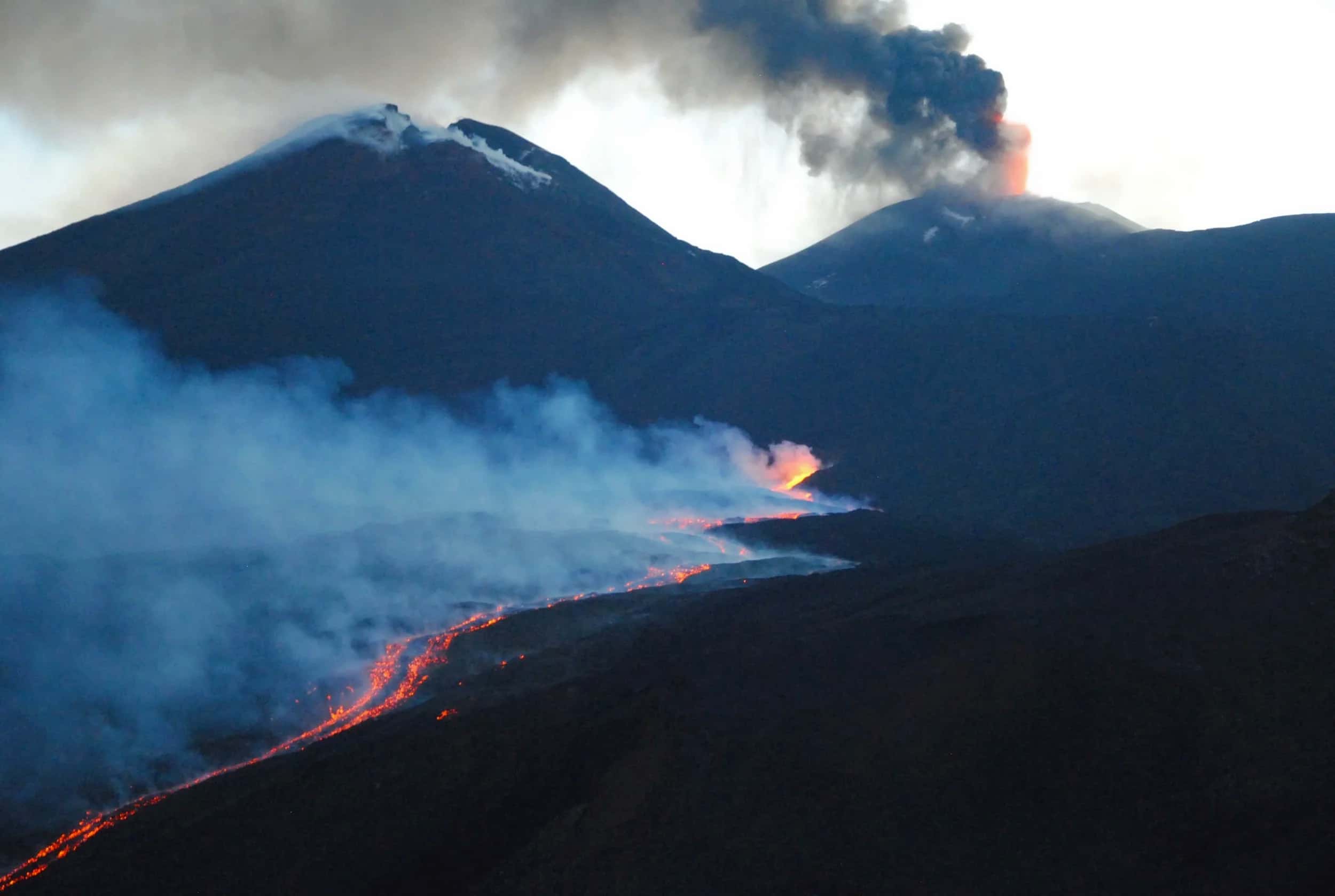 The lava flow running between the craters at dusk, among steam and smoke