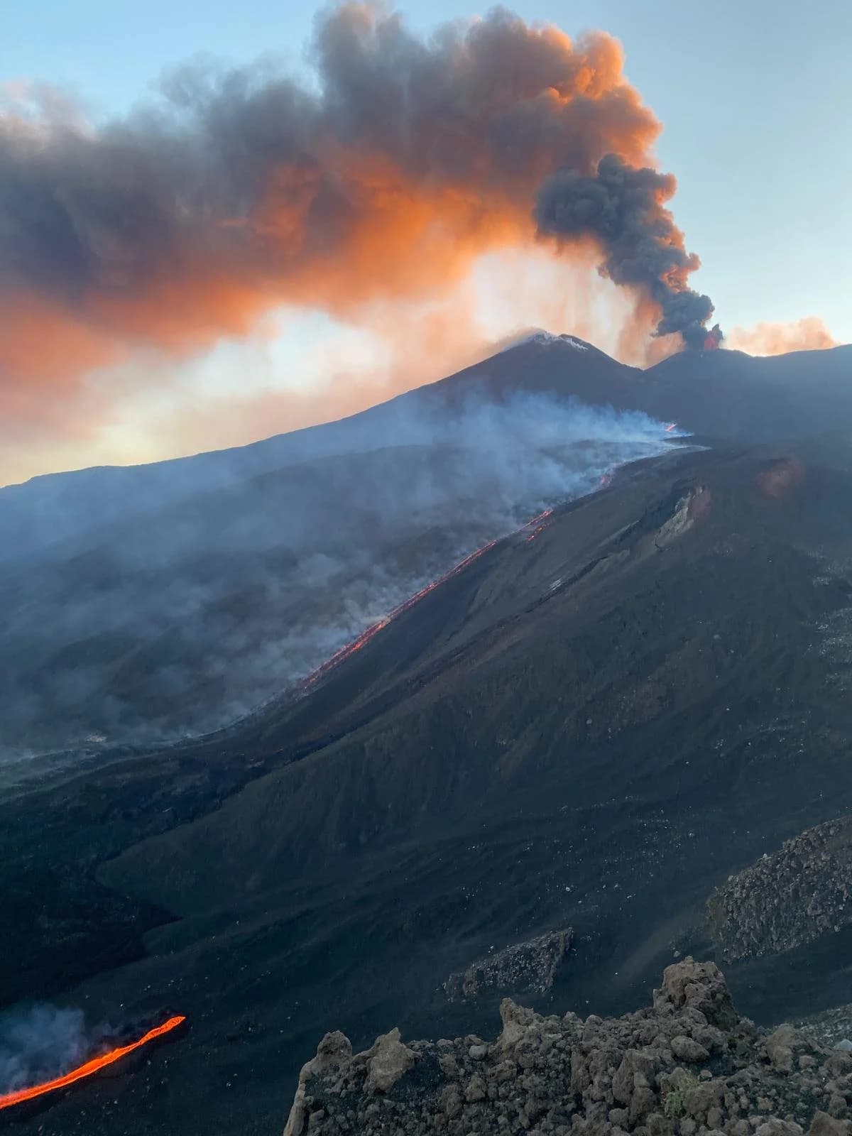 Colonna di cenere illuminata dal tramonto sopra il canale di lava