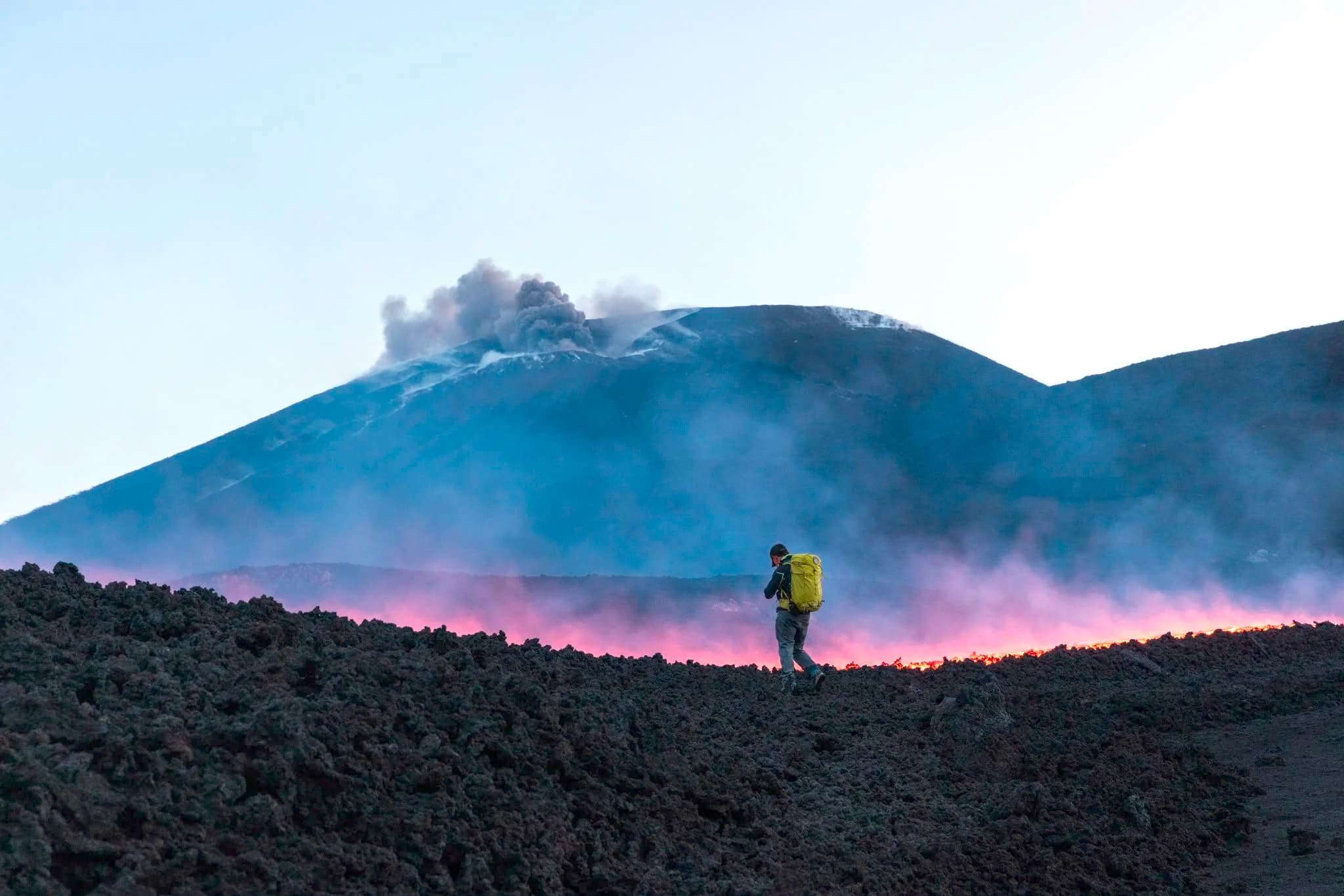 La guida con lo zaino giallo cammina davanti alla colata incandescente